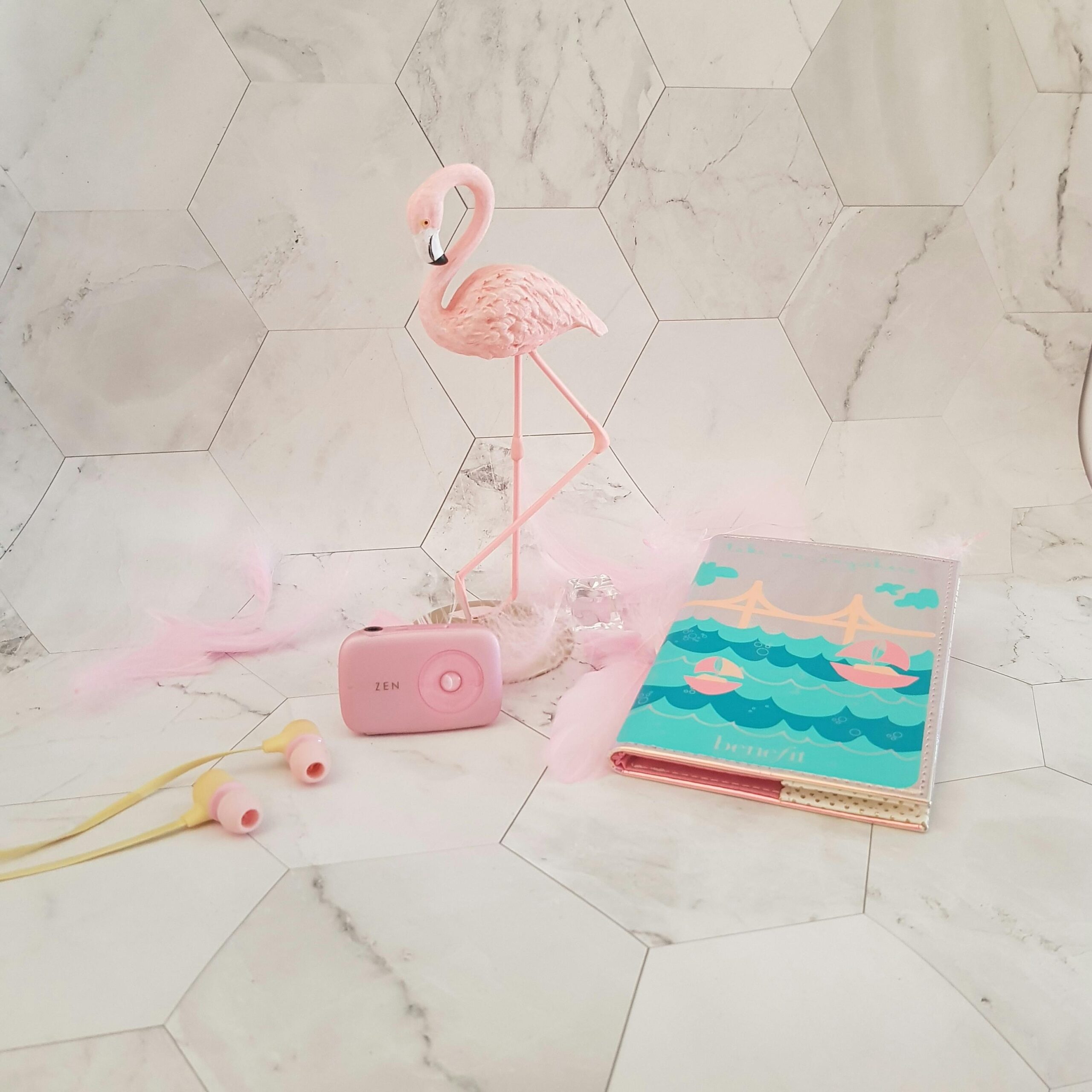 Charming pink flamingo decor with earphones and photo album on a modern hexagon tile floor.